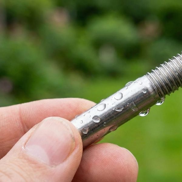 Nahaufnahme einer menschlichen Hand, die einen glänzenden Metall-Gewindestab hält. 
