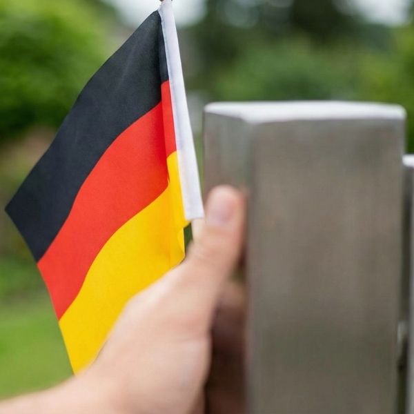Made in Germany: Eine Nahaufnahme im grünen Garten, die eine Hand zeigt, die eine kleine deutsche Nationalflagge an einem Metallstab hält.